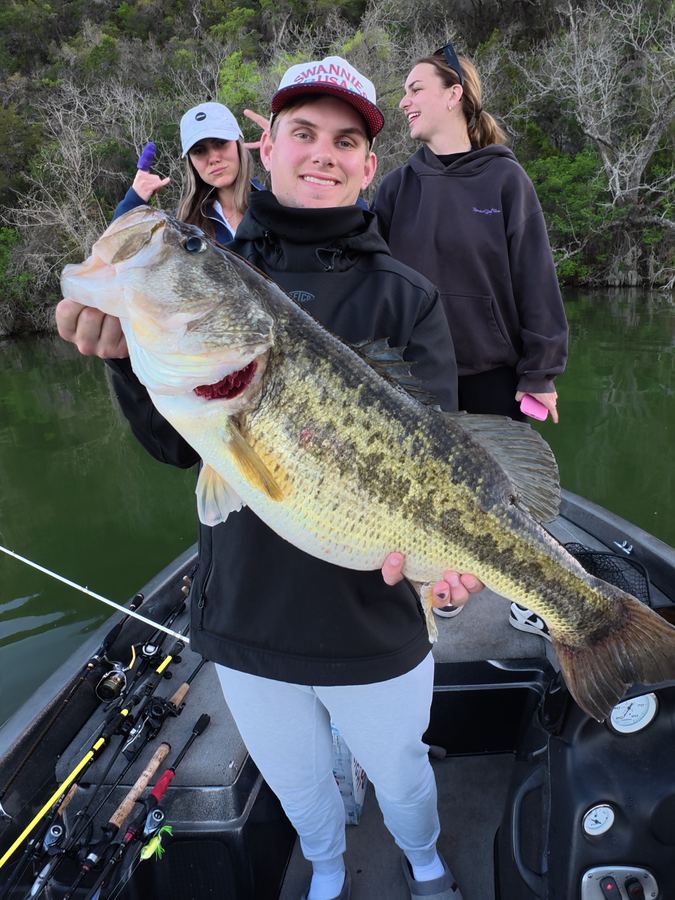 Young angler with a giant largemouth bass, friends laughing behind
